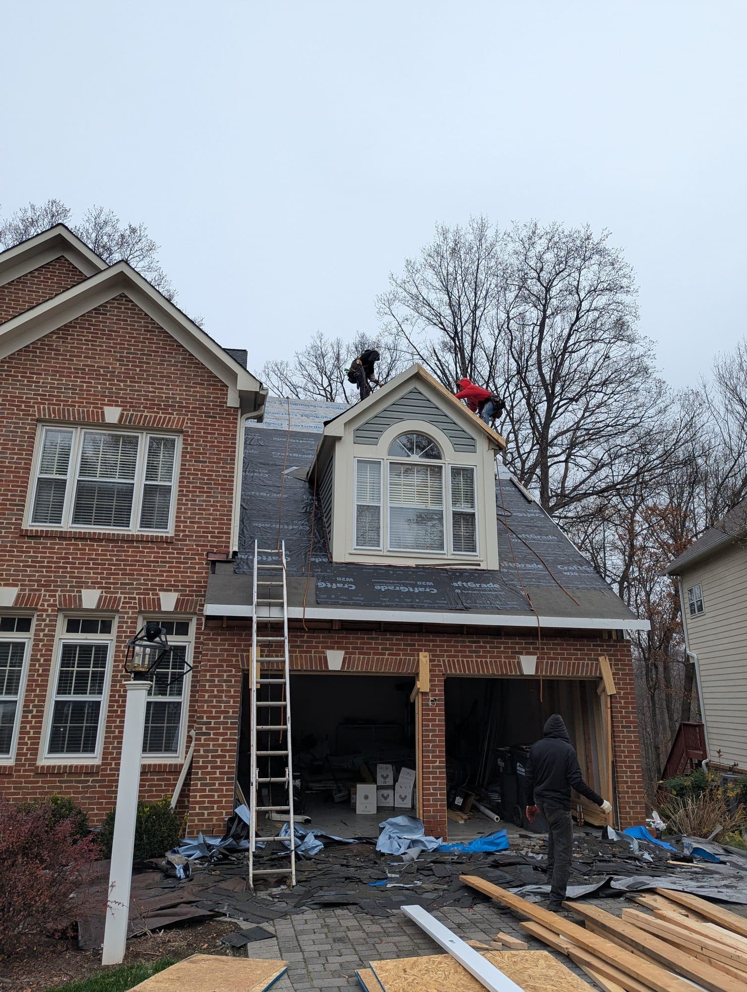 Roofing crew installing synthetic underlayment on a home's roof and dormer
