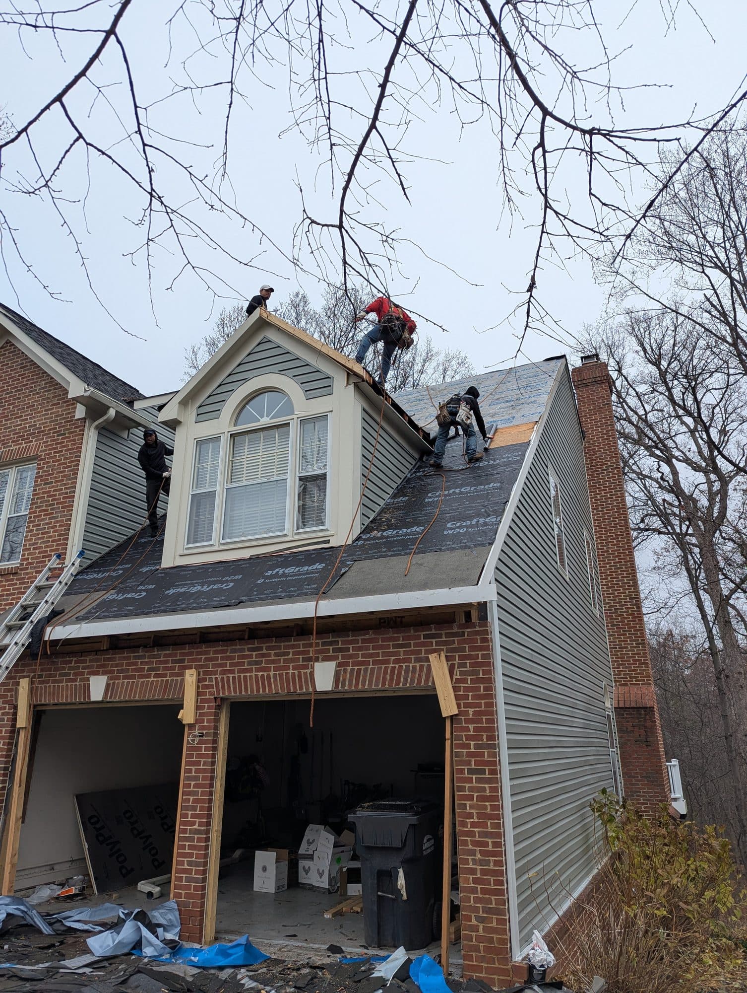 Roofing crew working on underlayment and flashing around a dormer and chimney