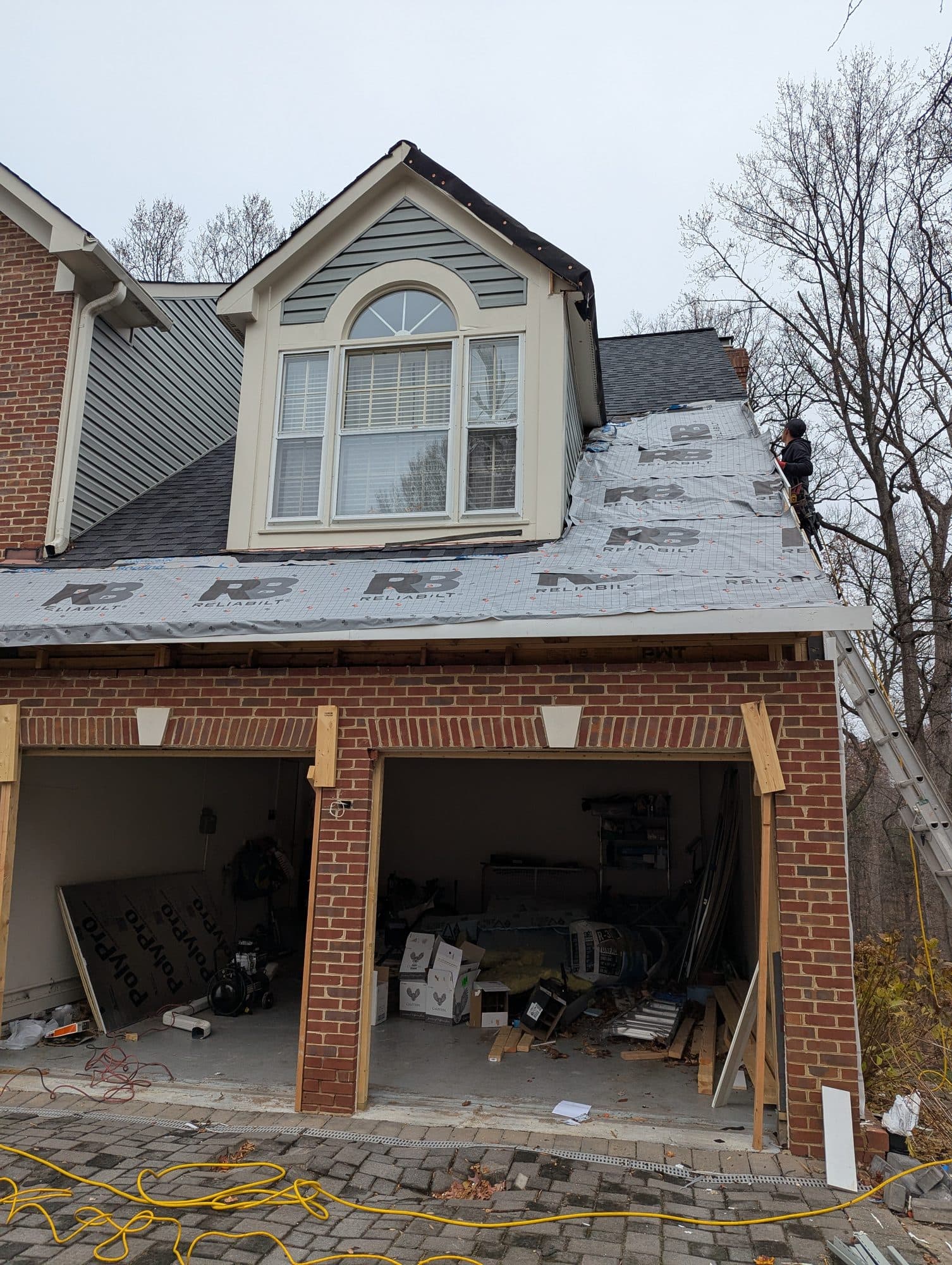 Wide view of a home with new roof underlayment installed and a roofer finishing a dormer
