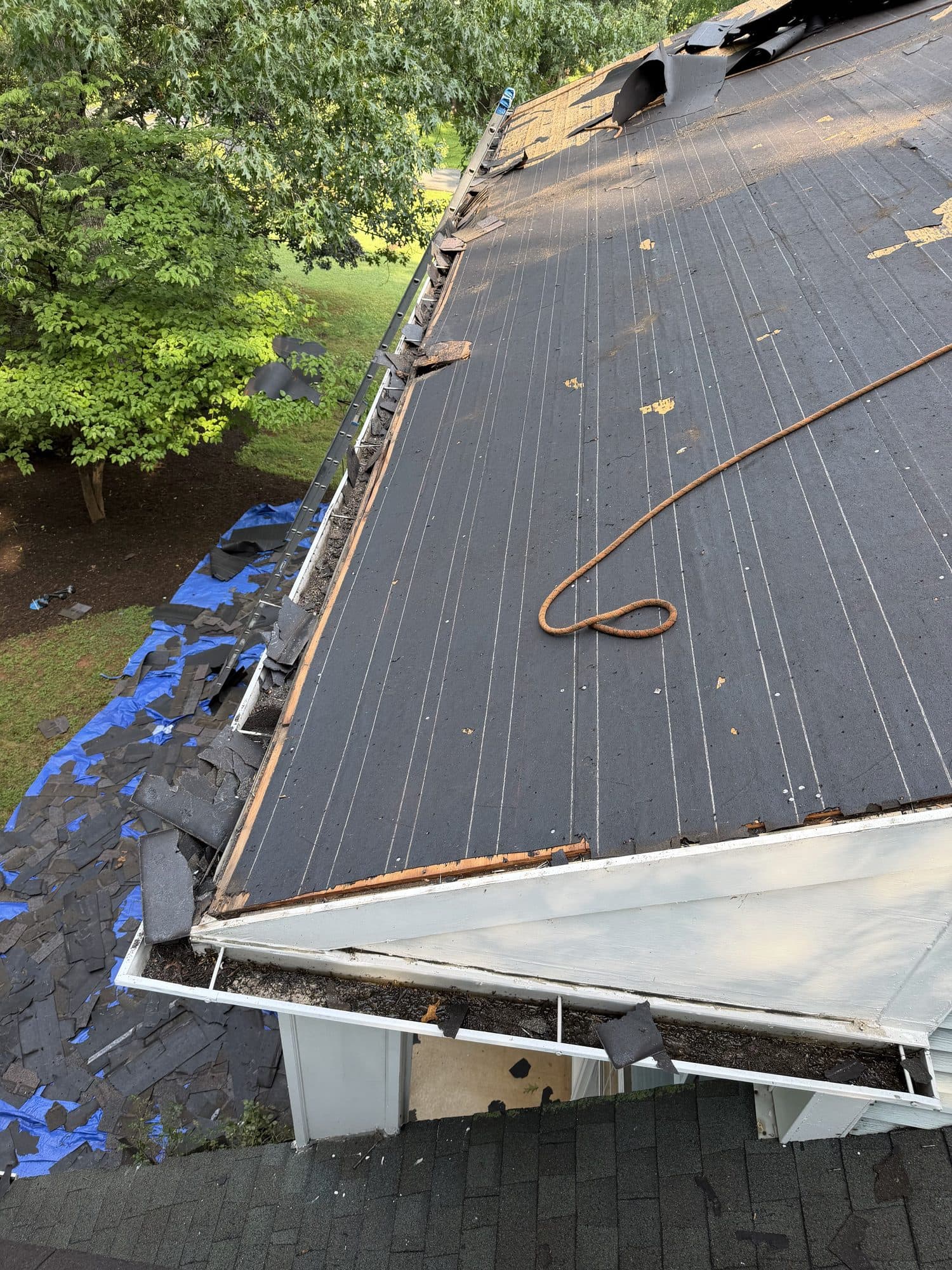 Close-up of a torn-off roof deck with old shingle debris on a tarp below